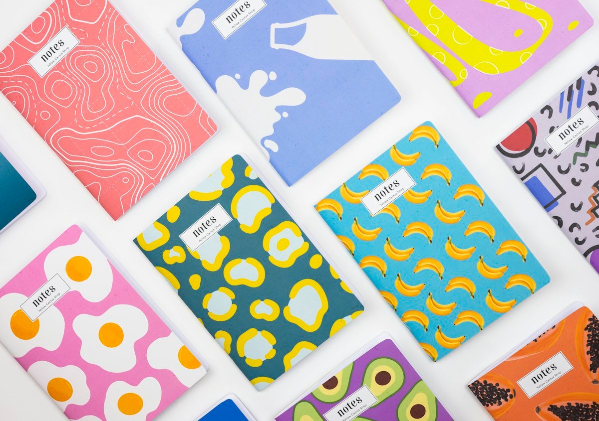 Many colourful patterned notebooks laid out on a white surface, each labelled notes